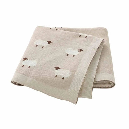 Couverture bébé brune en coton à motifs moutons, pliée sur fond blanc