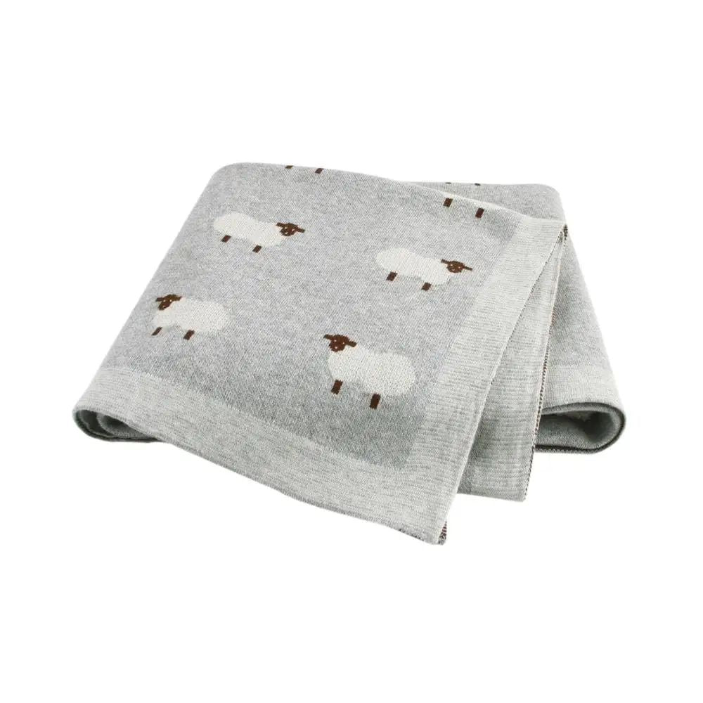 Couverture bébé grise en coton à motifs moutons, pliée sur fond blanc