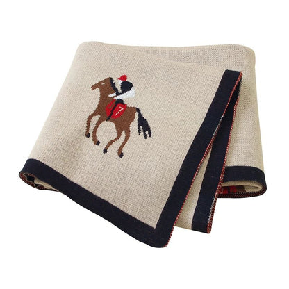 Couverture bébé brune en coton à motif cheval, pliée sur fond blanc