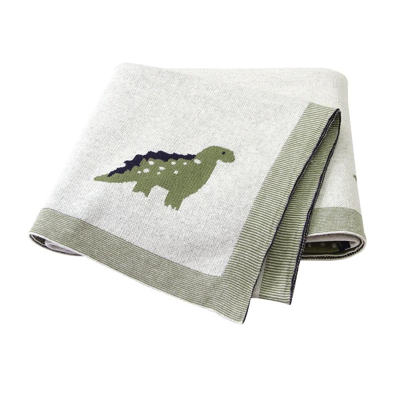 Couverture bébé verte en coton à motifs dinosaures, pliée sur fond blanc